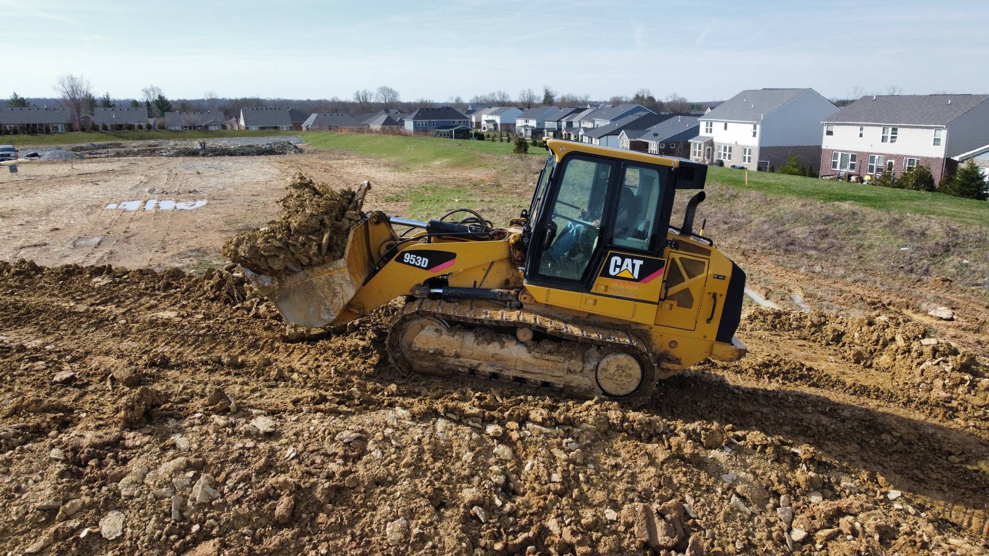 CAT 953D track loader carrying a bucket of dirt on a residential development site