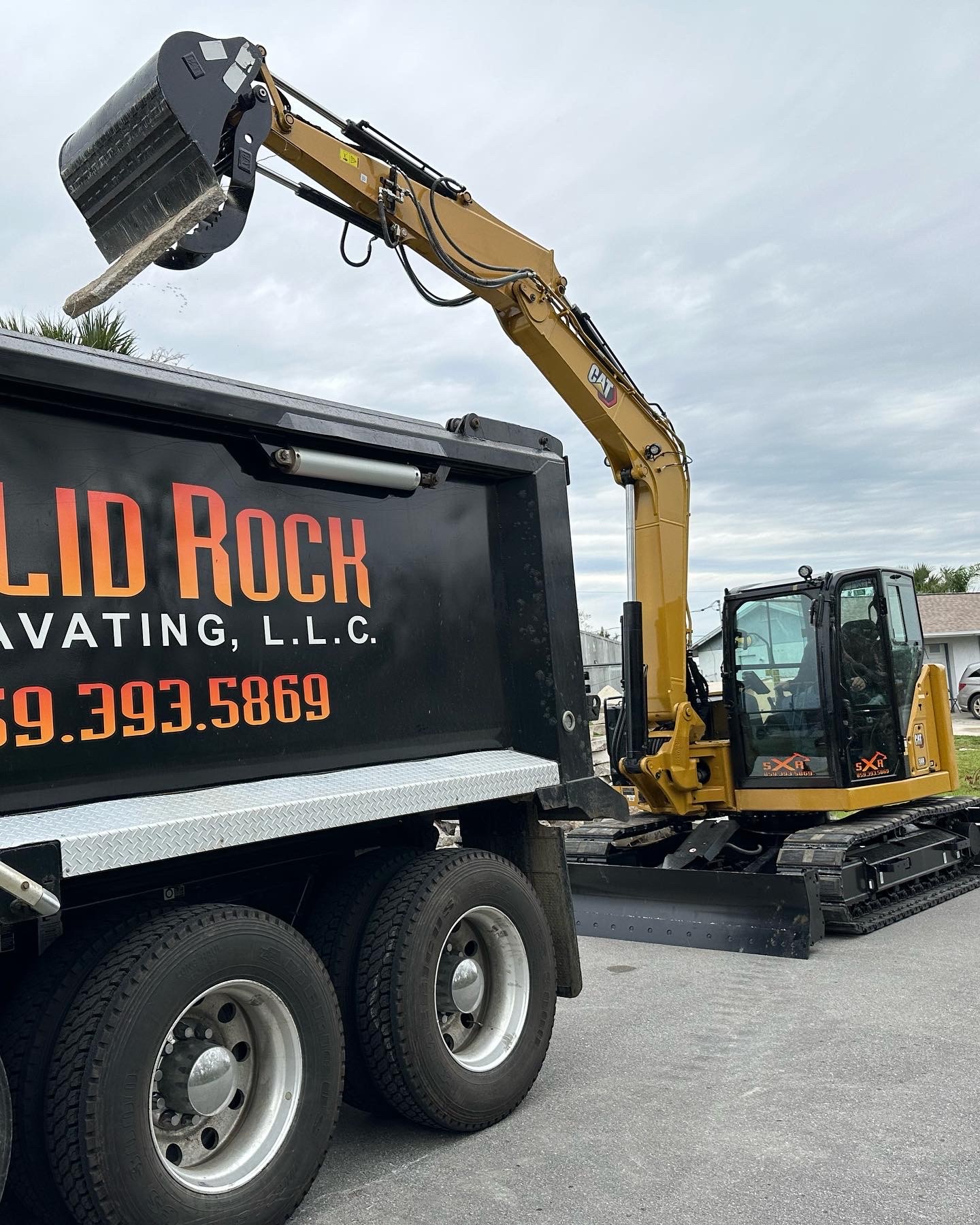 Solid Rock Excavating CAT excavator loaded on a lowboy trailer behind a dump truck